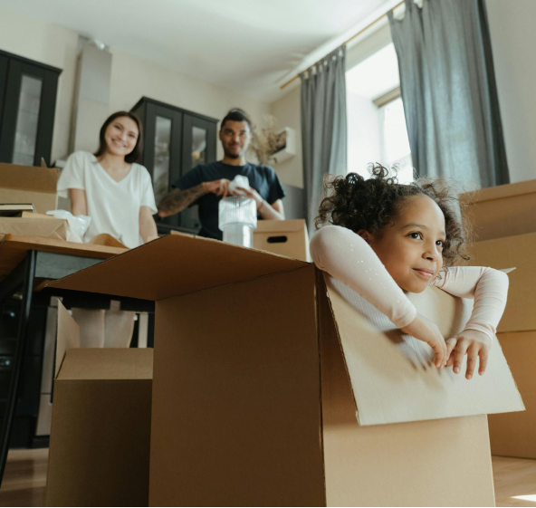 A little girl playing in an empty cardboard box with a man and a woman smiling at her.