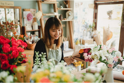 Woman surrounded by flowers, carefully placing some bouquets in boxes.